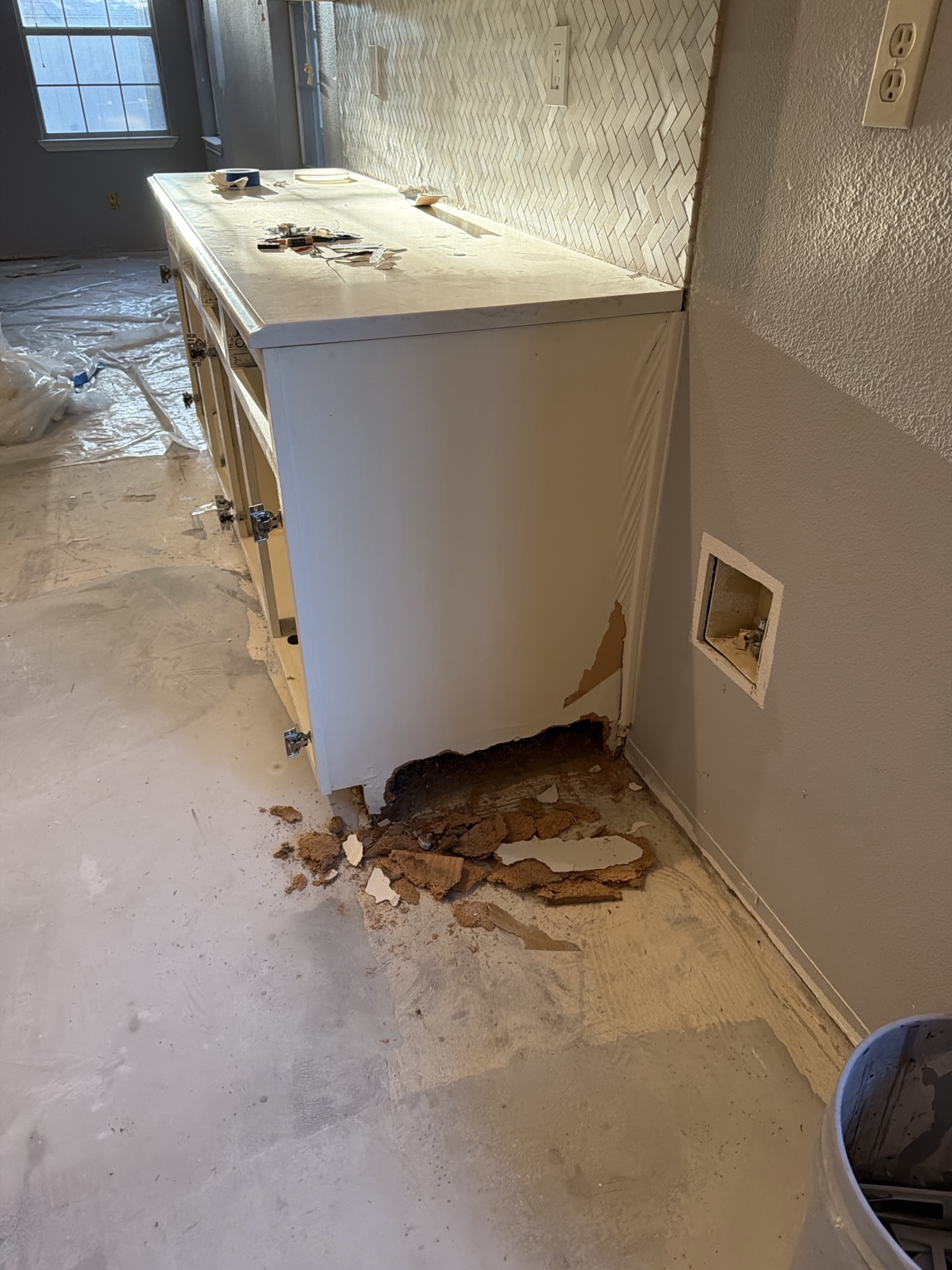Water-damaged lower end of a white base cabinet beside a wall opening